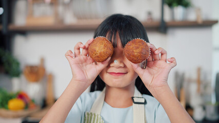 Portrait of asian little girl closing eyes by banana muffin cake smiling to camera. Cheerful asian...