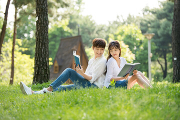 A young male and female couple are enjoying a pleasant picnic while drinking drinks and reading books on the forested park lawn.