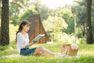The young woman is having a good time drinking drinks and reading books in a forested park.