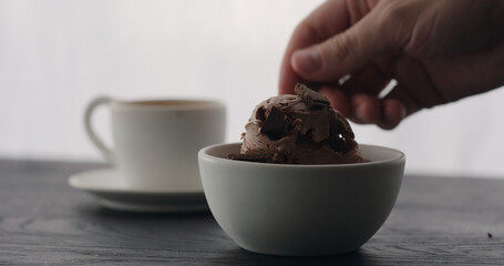 put chocolate pieces on chocolate ice cream into white bowl with espresso on black wood table