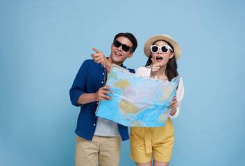 Happy Asian couple tourist looking map and hand pointing to copy space with baggage going to travel...