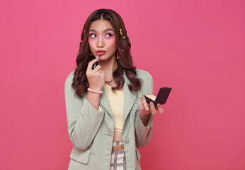 Makeup lipstick woman ready looking in pocket mirror. beautiful trendy young asian female fashion model putting makeup on pink background.