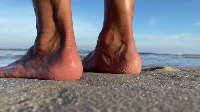 Close up view back of male heel feet standing on sand seashore sunny day. Walking towards the ocean in slow motion. Back view.
