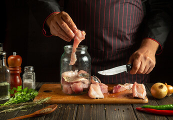 A man prepares herring from fish steaks and aromatic spices on the kitchen table. The concept of canning sea fish in a jar with salt and coriander