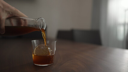 pour cold brew coffee over ice ball in tumbler glass on walnut table