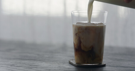 pour milk into ice coffee on black wood table