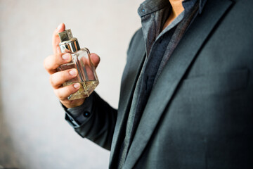 Handsome man in a suit applying perfume on neck against light background at home. Male holding up...