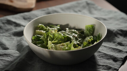 man mixing dressing over romaine leaves in white bowl