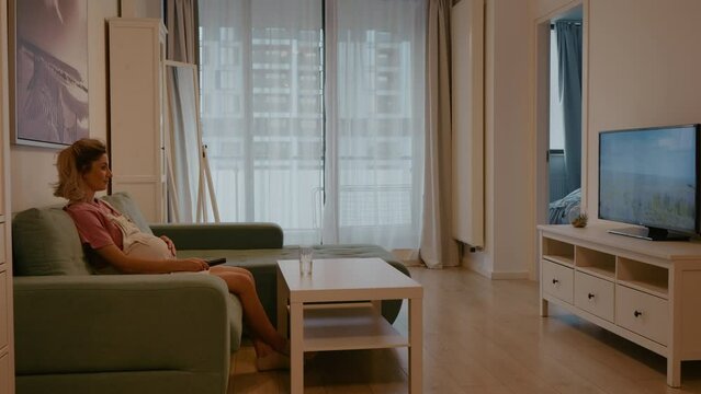 Beautiful pregnant woman watching movie alone sitting on the sofa. Sitting at home enjoying the self time. Happy Family Concept