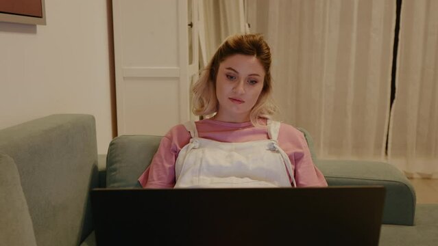 Portrait of pregnant woman interested in watching laptop smiles when the baby kicks. Pregnant woman using laptop at home. Pregnancy concept.