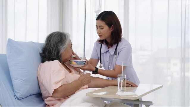 A nurse provides food and water to an elderly Asian patient who is unable to help himself.
