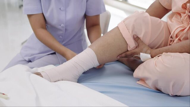 Close-up photo of an Elderly Asian patient admitted to hospital A nurse cares for a patient's injured leg bandage.
