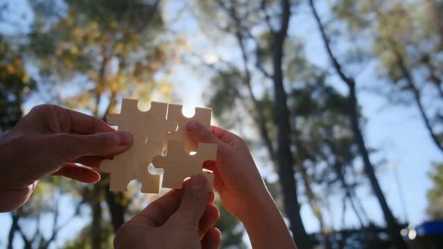 Diverse hands collaborate in assembling puzzle pieces, symbolizing teamwork, problem-solving, and creative solutions. Fingers delicately hold and connect puzzle pieces, showcasing the collective.