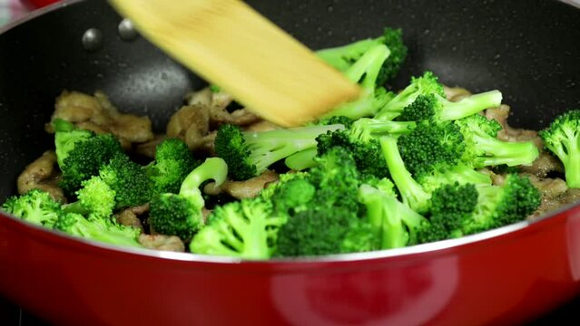 Woman cooking a delicious Chinese meal of pork and broccoli in a red skillet on the stove in the kitchen