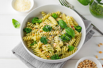 Vegetarian pasta with pesto sauce, broccoli, parmesan cheese and pine nuts on a white wooden background. Healthy food.