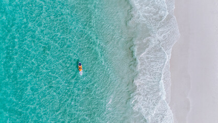 overhead drone view of a person on his stand up paddle board in the sea with green water on the beach with the whitest sand in the world in Jervis Bay, Australia on a daylight morning on vacation
