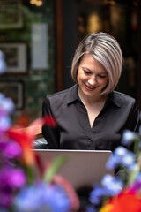 A young business woman is working on a laptop, sitting in a chair in a public place. 