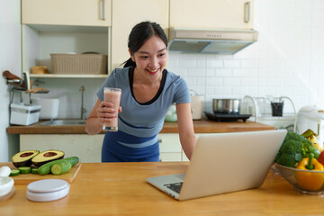 Young woman in Asian exercise clothes making a fruit and vegetable smoothie after a healthy workout at home. Concept of diet and healthy food, lifestyle