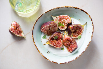 Green bowl with fresh torn fig fruits and white yogurt, horizontal shot on a beige granite background, elevated view