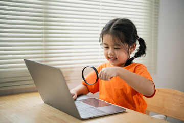 Asian baby kid girl holding magnifying glass and using laptop education to get good ideas, children and school concept - happy smiling student girl learning studying. Education development concept.