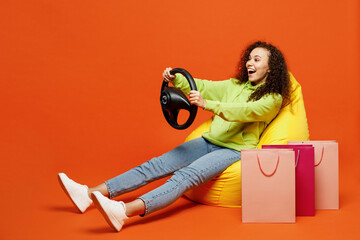Young excited woman wearing green casual clothes sit in bean bag chair hold steering wheel near...