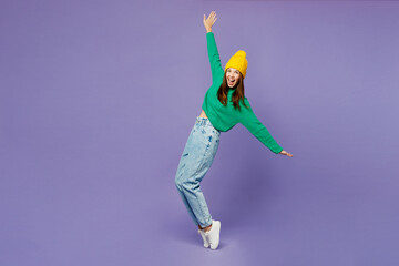 Full body young woman wear green sweater yellow hat casual clothes stand on toes lean back with outstretched hands isolated on plain pastel light purple background studio portrait. Lifestyle concept.