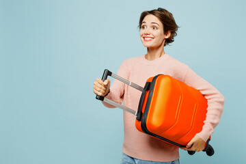 Traveler smiling happy woman wears sweater casual clothes hold bag suitcase isolated on plain blue...