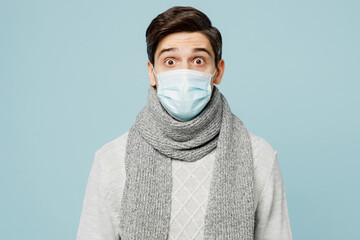 Young surprised ill sick man wear gray sweater scarf sterile mask look camera isolated on plain...