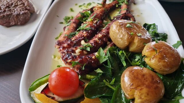 A traditional Portuguese dish of potato octopus with tomato and spinach called polvo a lagareiro close-up on a white plate