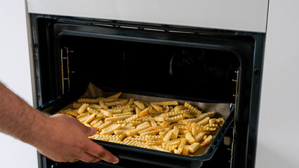 Caucasian man opening an oven and putting frozen french fries inside - 680558453
