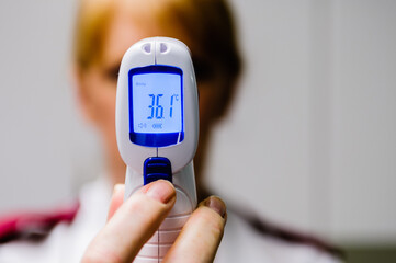 A ward sister nurse shows a patient their temperature read by an infra-red forehead heat detector