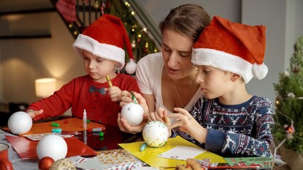 Young mother teaching her children how to make traditional Christmas decorations and baubles