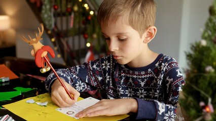 Closeup of little boy writing a letter to Santa in a living room decorated for Christmas