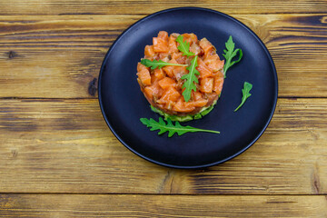 Salmon tartare with avocado and arugula on wooden table. Top view