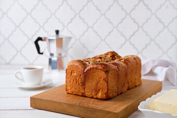 Butter brioche bread sprinkled with almond petals on a wooden board on a light concrete background. Wheat bread recipes.