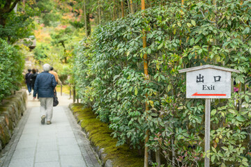 Exit direction wooden signboard (English and Japanese text) in Japanese gardening environment. Sign and symbol object photo.