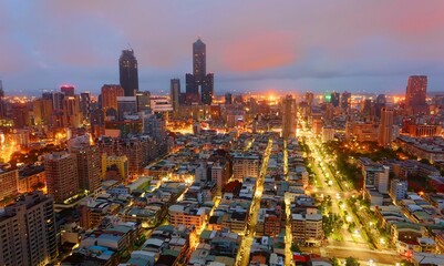 Aerial view of Kaohsiung City at dusk, a vibrant seaport in South Taiwan, with the famous landmark 85 Sky Tower standing by the harbor in background and street lights dazzling in blue evening twilight