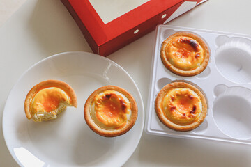 Top view of some delicious Chinese custard egg tarts (danta) taken out of box, two on a plate, one bitten. A custom snack dessert popular across China, originating from Guangzhou