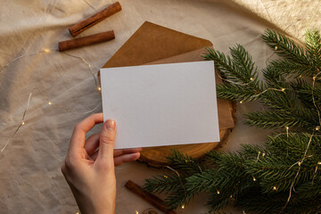 Template for Christmas greeting card. Hand holds empty sheet of paper with Christmas tree branch and cinnamon sticks on background. Mock up for New Year postcard