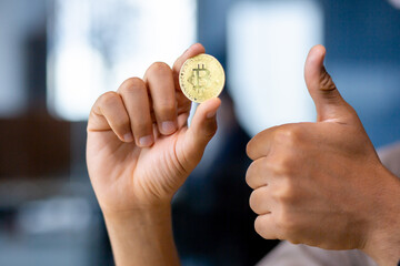 Close-up portrait of hands holding bitcoin virtual currency and showing like thumbs up, office space.
