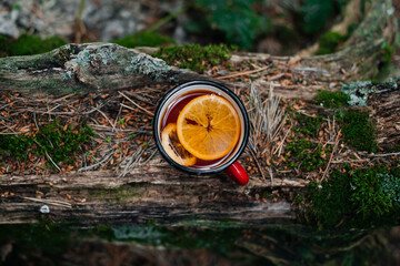 a red mug of tea stands on a log in the forest
