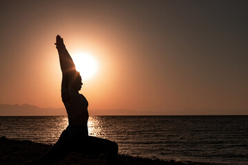 Woman performing warrior pose yoga on the beach at sunrise