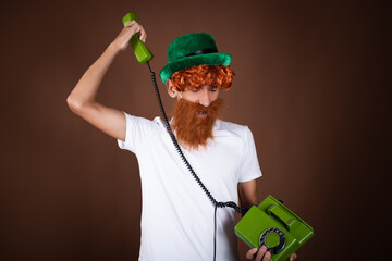 St.Patrick 's Day. Funny guy in a leprechaun costume posing on a brown background.