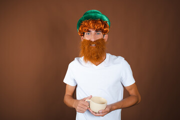St.Patrick 's Day. Funny guy in a leprechaun costume posing on a brown background.