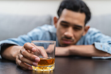 melancholy young Asian man drinks alcoholic whisky alone at home feeling dizzy after drunk - obrazy, fototapety, plakaty