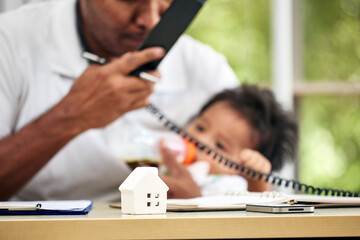Young Asian father holding calling telephone and treat baby boy feeding milk and working from home...