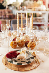 elegant Christmas table setting with trendy plates, candles and golden cutlery, gold accessories