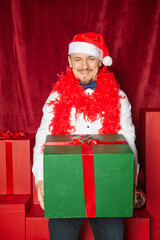 Young handsome man wearing Santa hat holding heavy Christmas gift box. New Year style