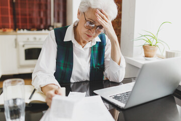 Portrait of upset stressed depressed senior caucasian woman in glasses looking at utility bill,...