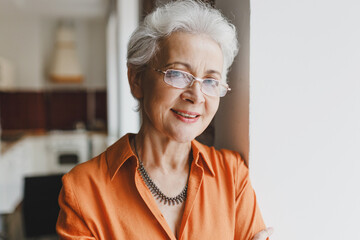 Closeup indoor portrait of elderly wise kind female grandmother in glasses with gray hair in orange...